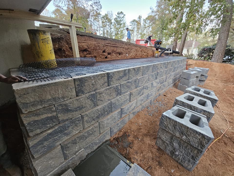 Construction site with stone wall, workers, and gray concrete blocks on the ground.