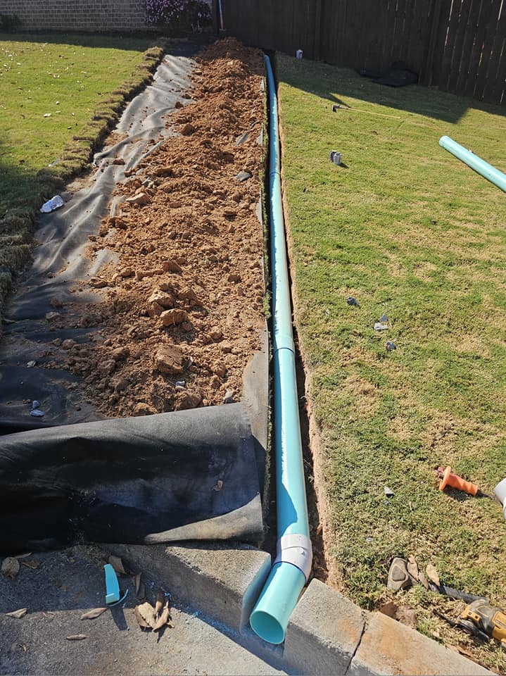 Newly installed blue drainage pipe in a trench along a grassy lawn.