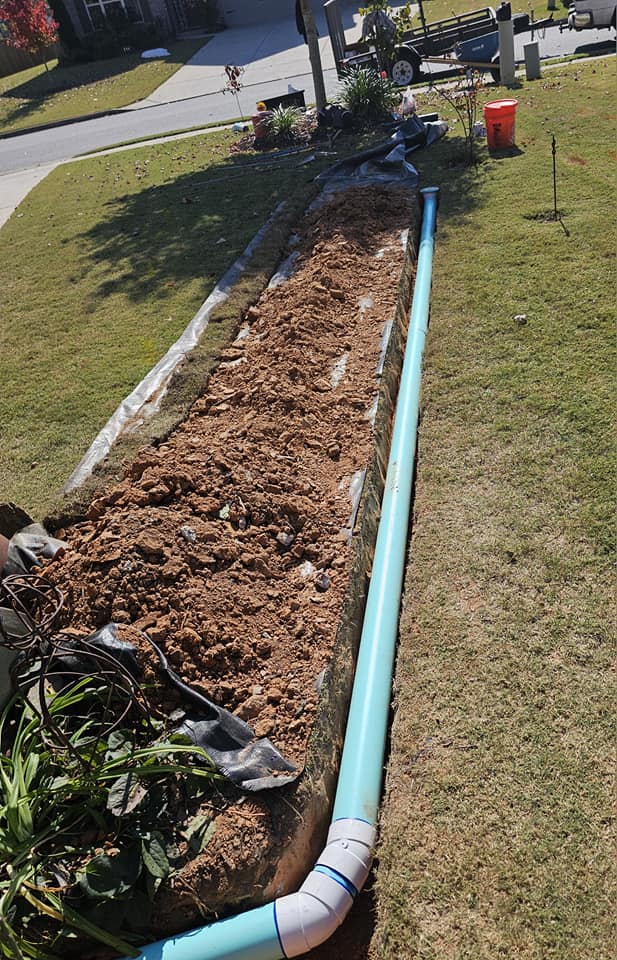 Trenched yard with blue drainage pipe installed alongside freshly dug soil and landscaping.