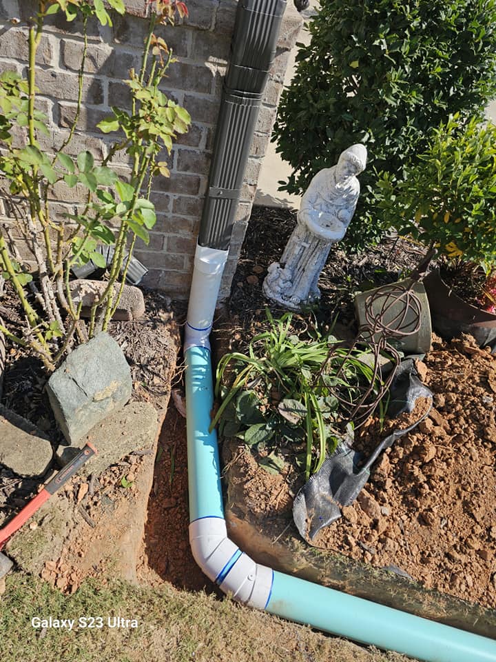 Blue drainage pipe installed next to a garden statue and shrubs in a landscaped yard.