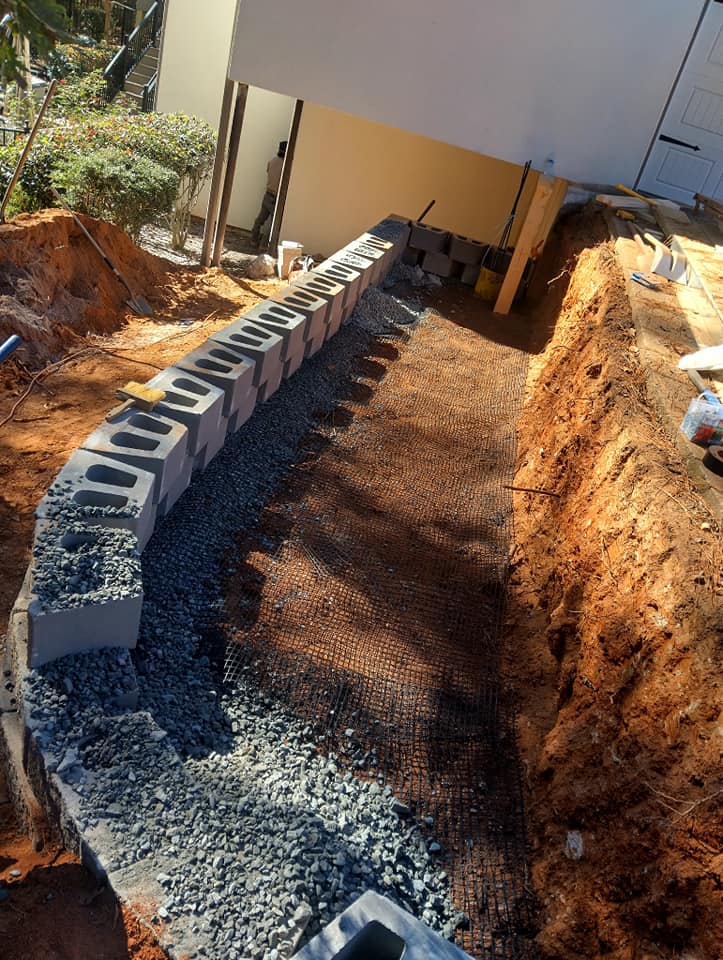 Construction site with stone blocks, gravel base, and foundation preparation in progress.