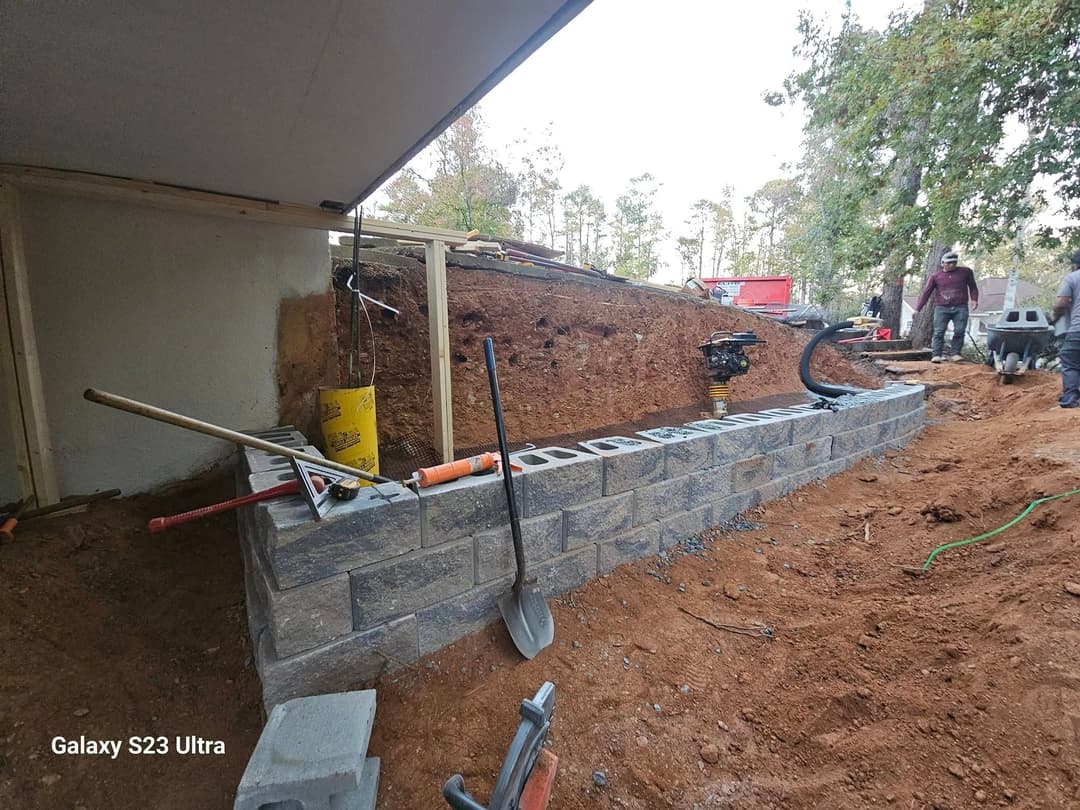 Construction site with a stone wall, tools, and workers building a landscape feature.