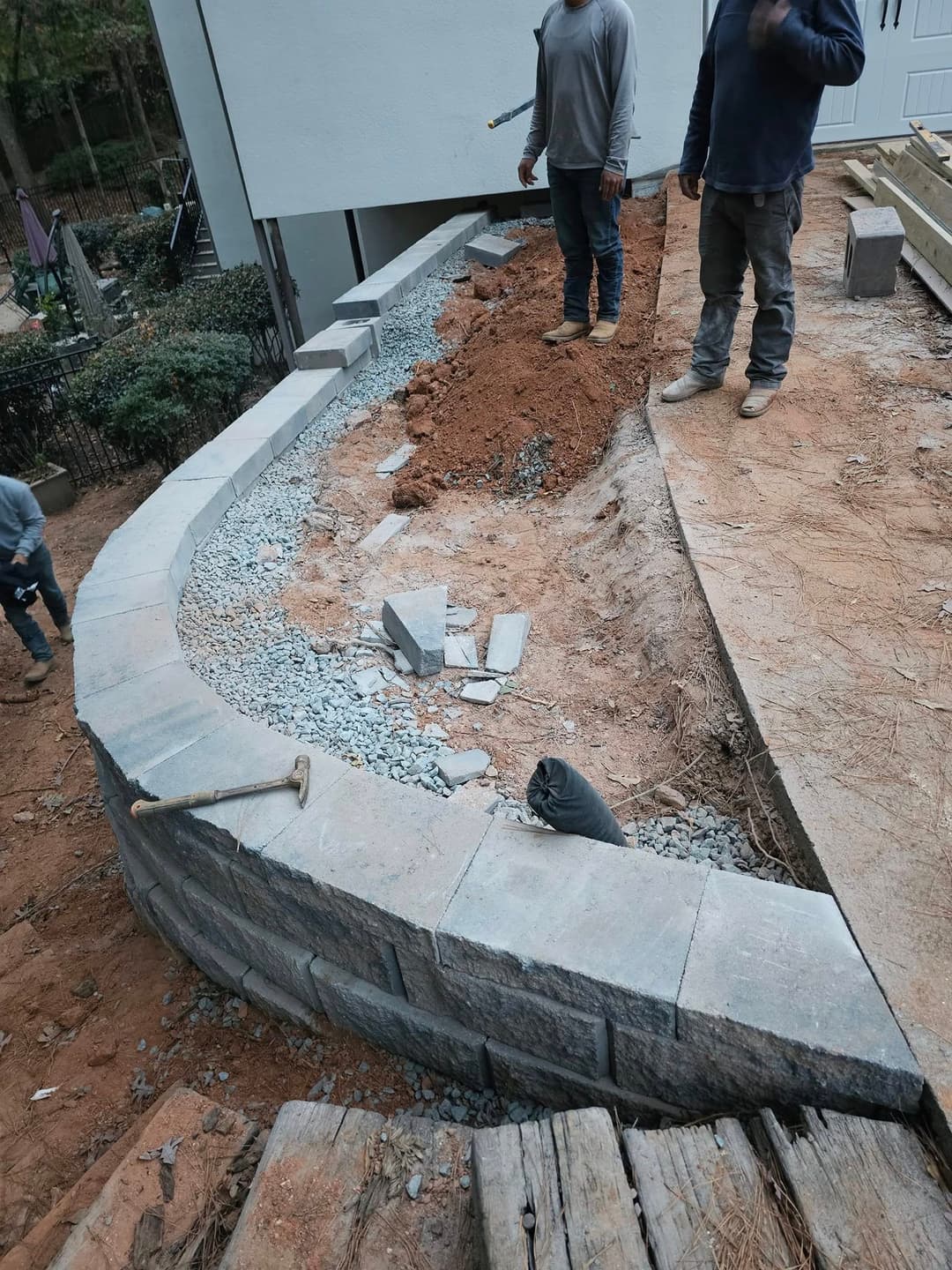 Workers constructing a stone retaining wall in a landscaped area with gravel base.