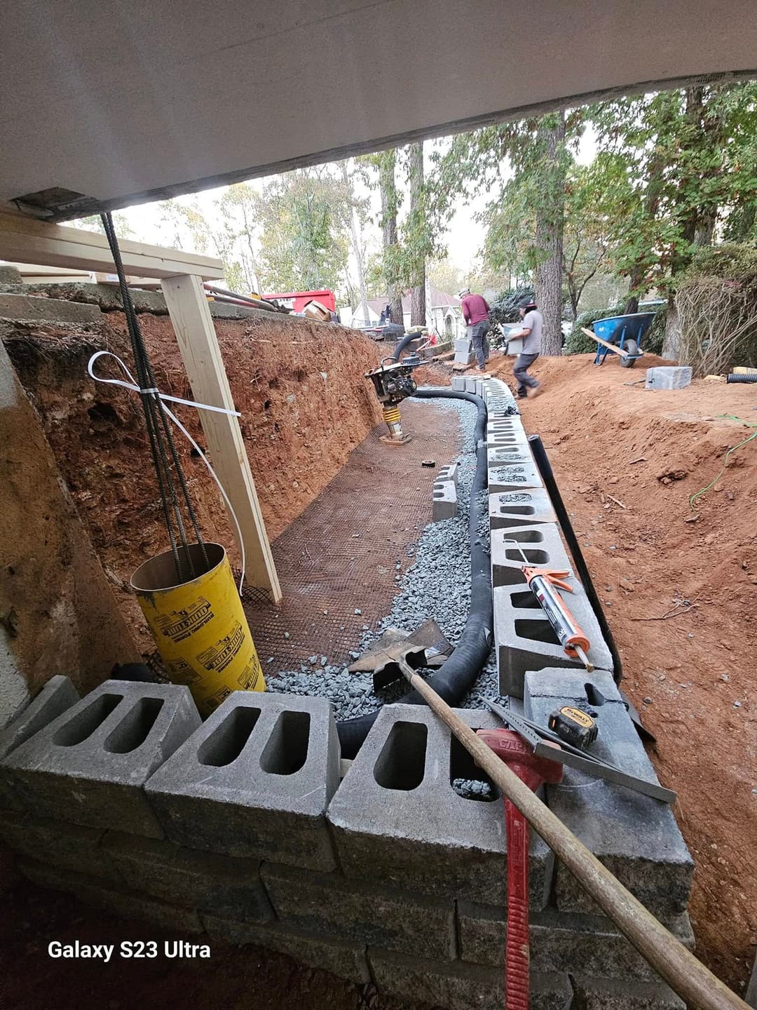 Construction workers installing drainage system with retaining wall blocks in a landscaped area.
