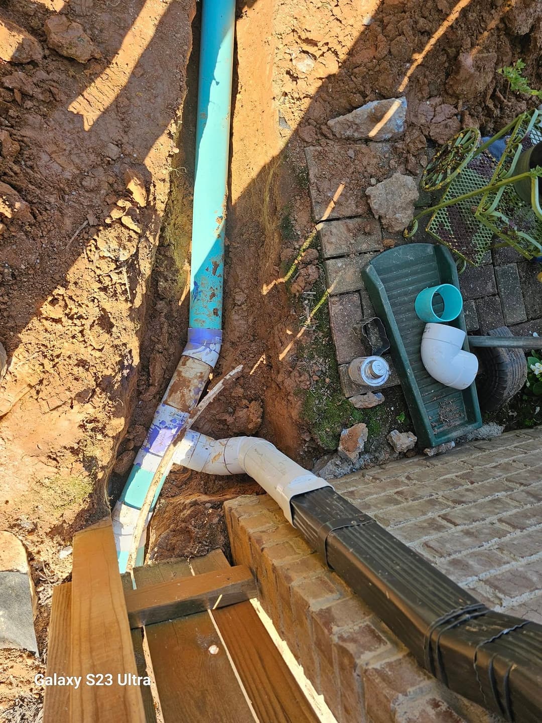 Trenched area showing blue and white drainage pipes installed near a brick foundation.