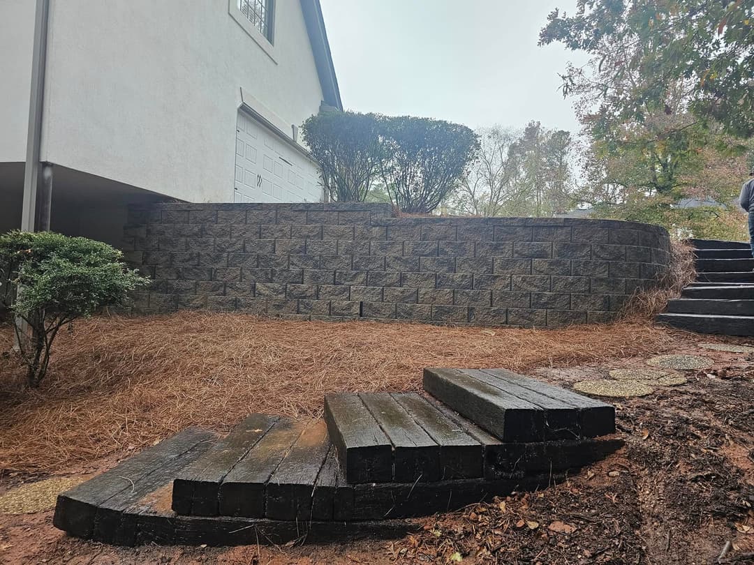 Wooden steps leading to a landscaped yard with stone wall and shrubs on a rainy day.