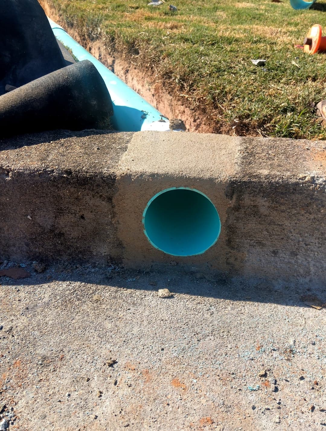 Blue PVC pipe embedded in concrete, with grass in the background at a construction site.