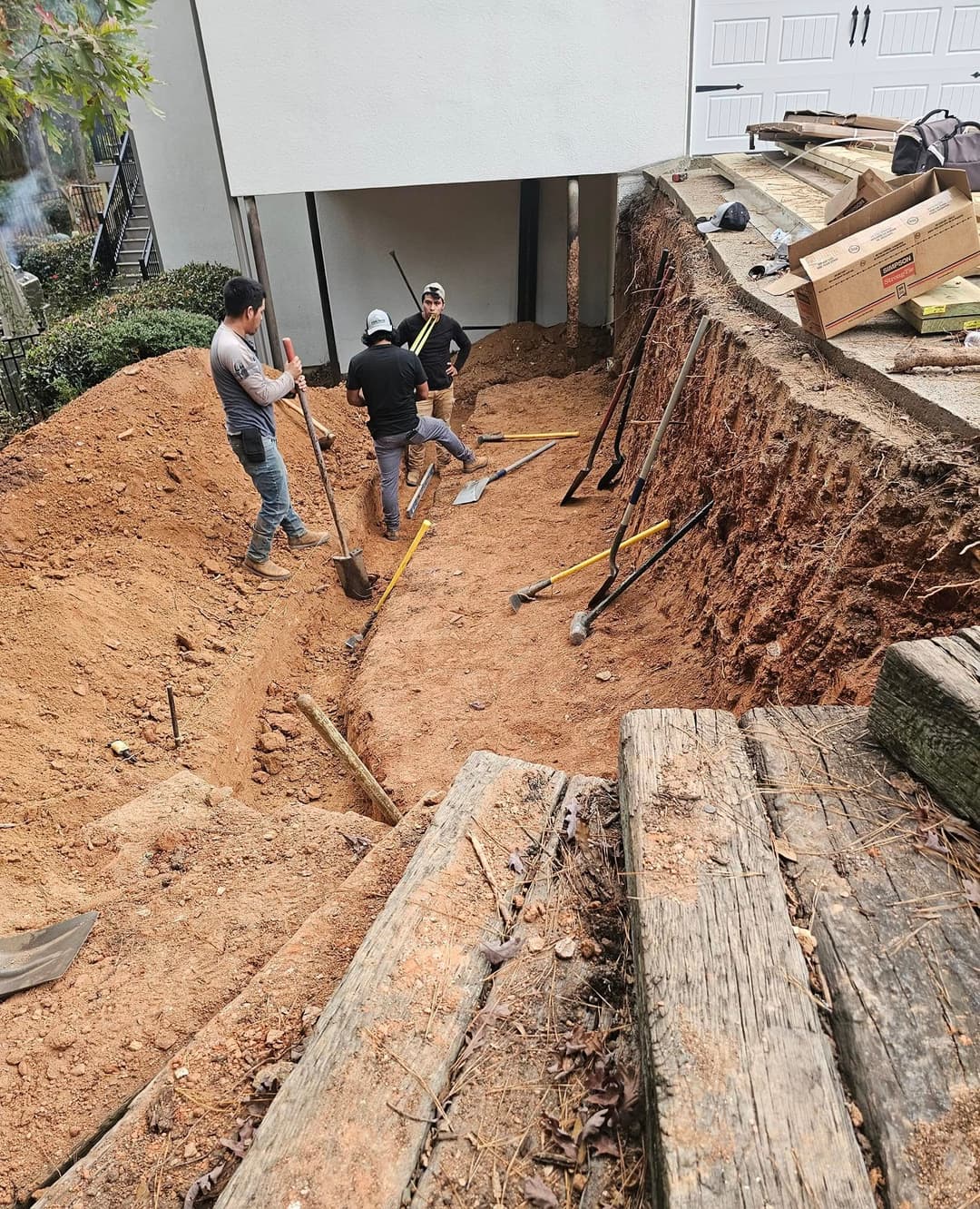 Construction workers excavating a deep trench in a residential backyard.