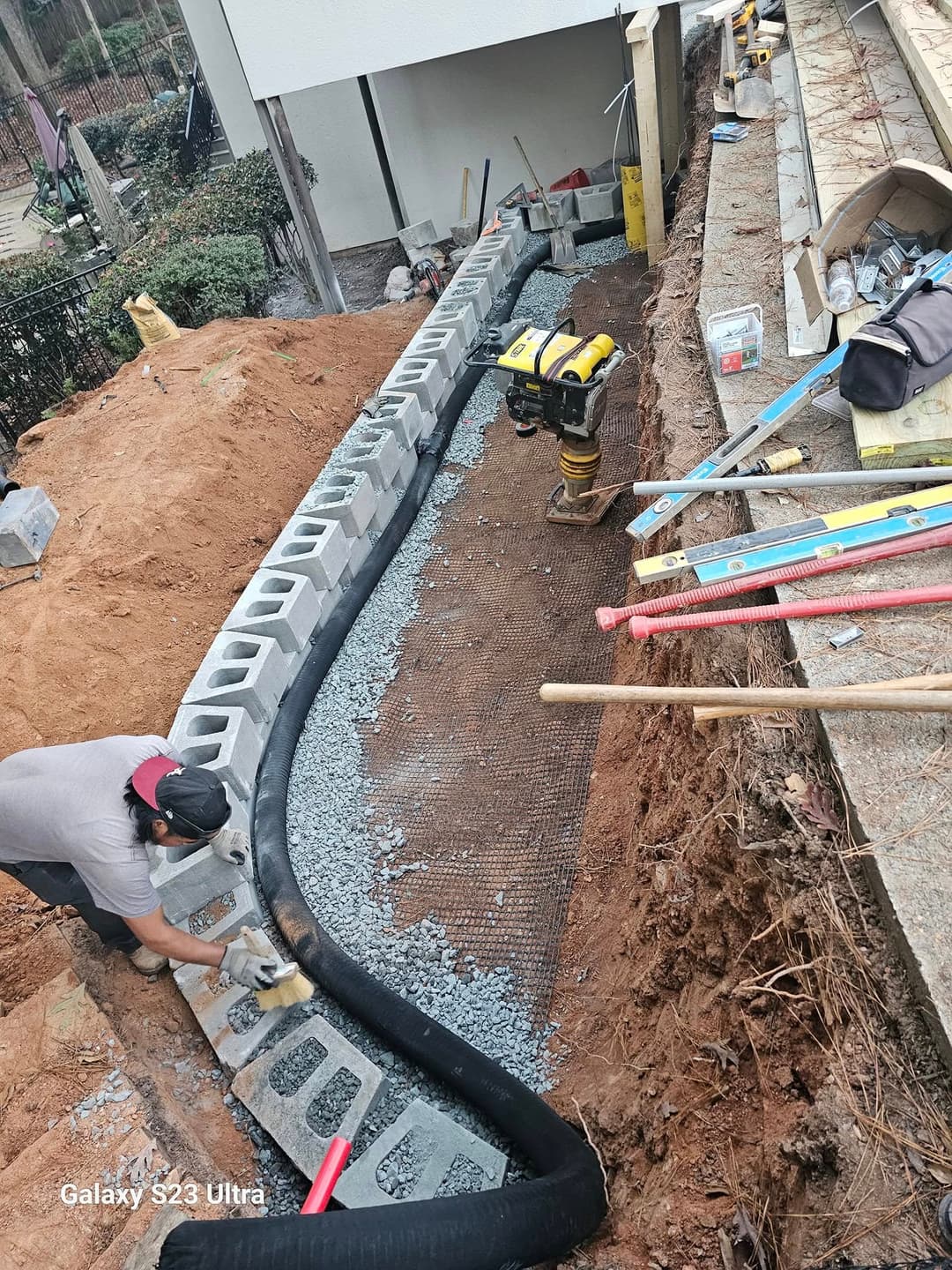 Construction site with concrete blocks arranged for drainage, tools and gravel visible.