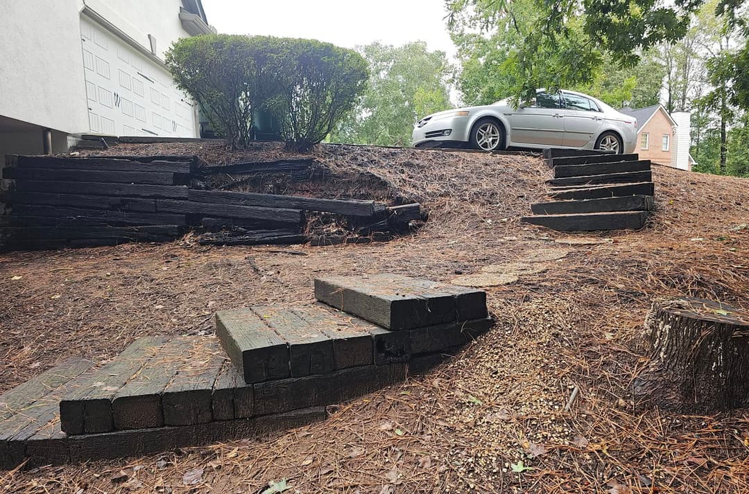 Stone steps lead up a hillside with a parked silver car and green shrubbery nearby.