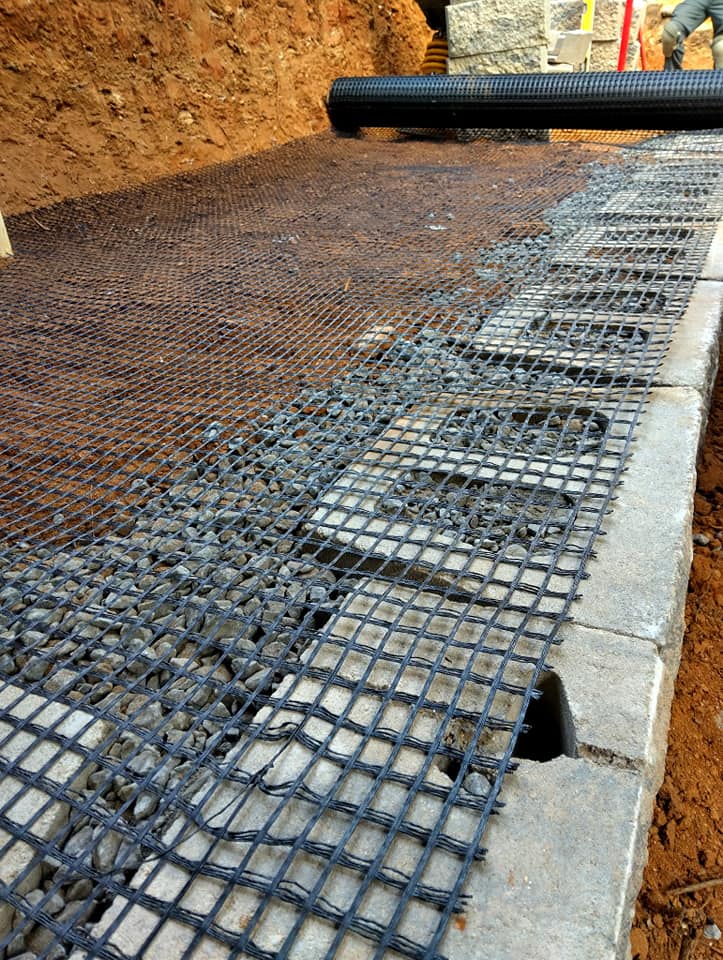 Geogrid installation over gravel for ground stabilization in construction site.